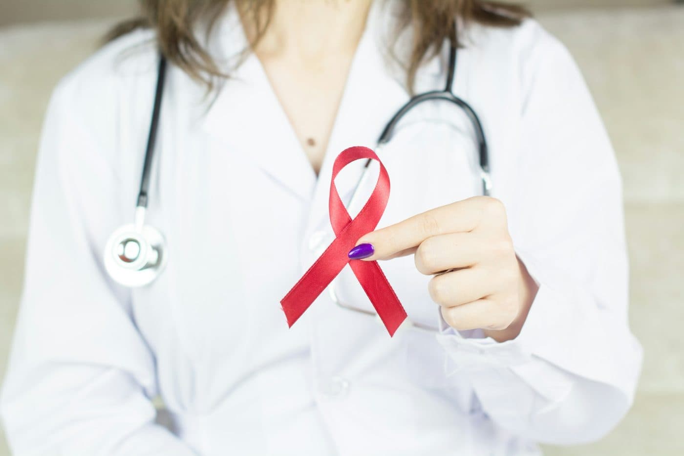 A clinician in a white coat holding a red awareness ribbon