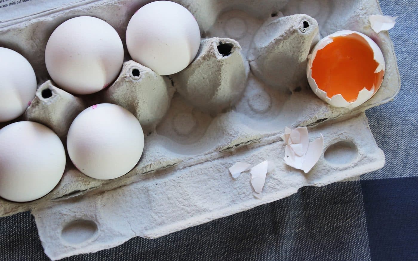 A carton of eggs with one shell opened to show the yolk