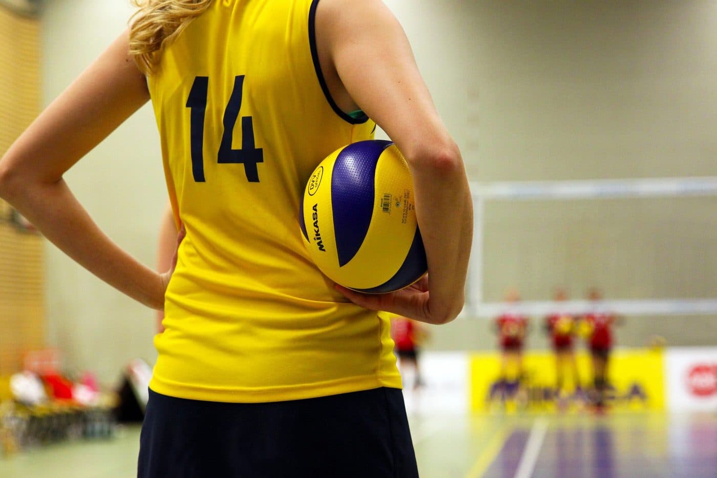 A young volleyball player holding a ball on an indoor court