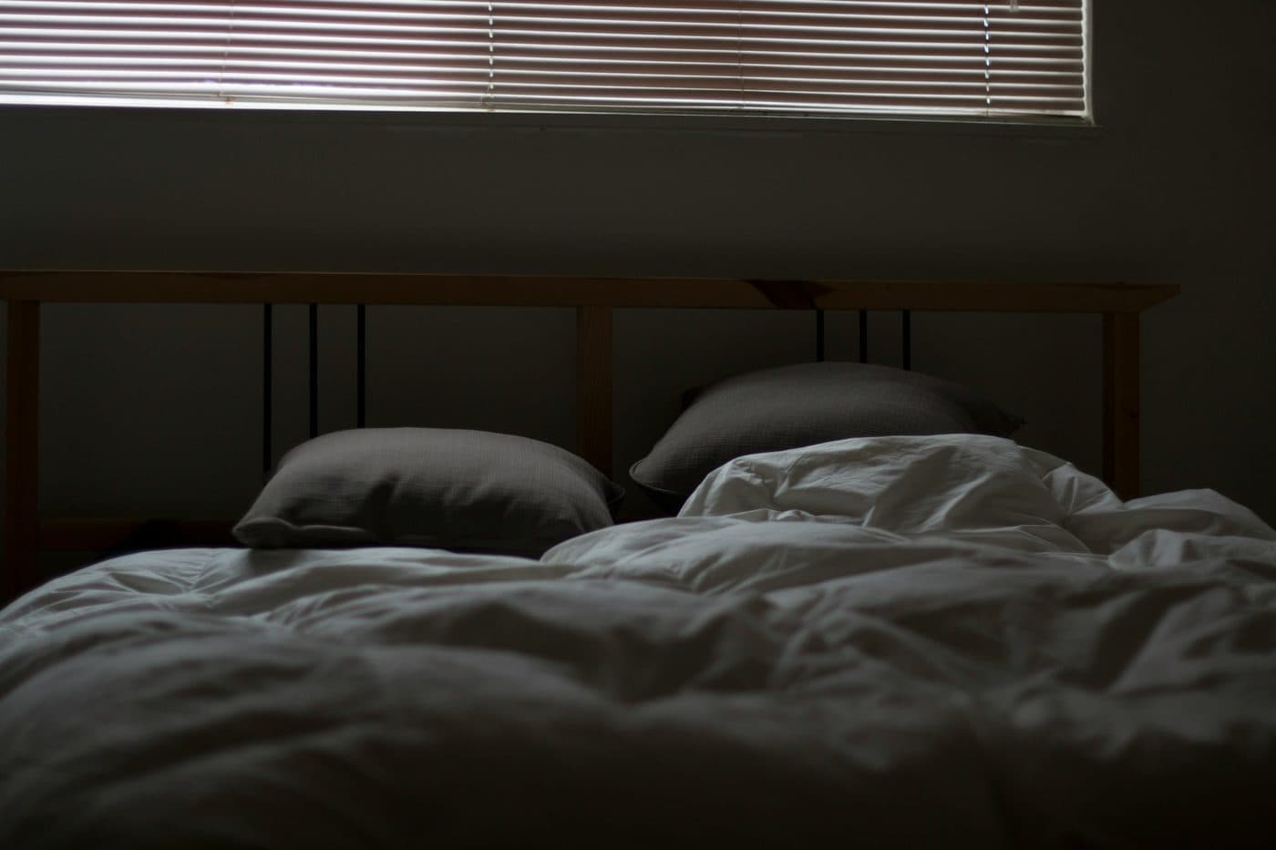 An empty, unmade bed in a darkened bedroom