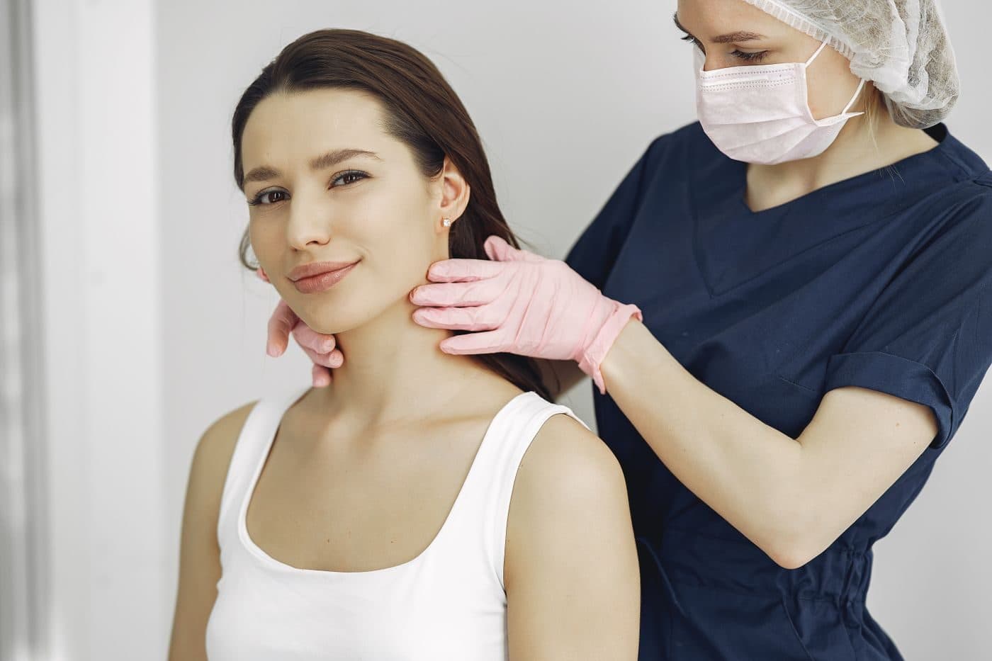 A clinician gently palpating a patient's neck to examine the thyroid gland