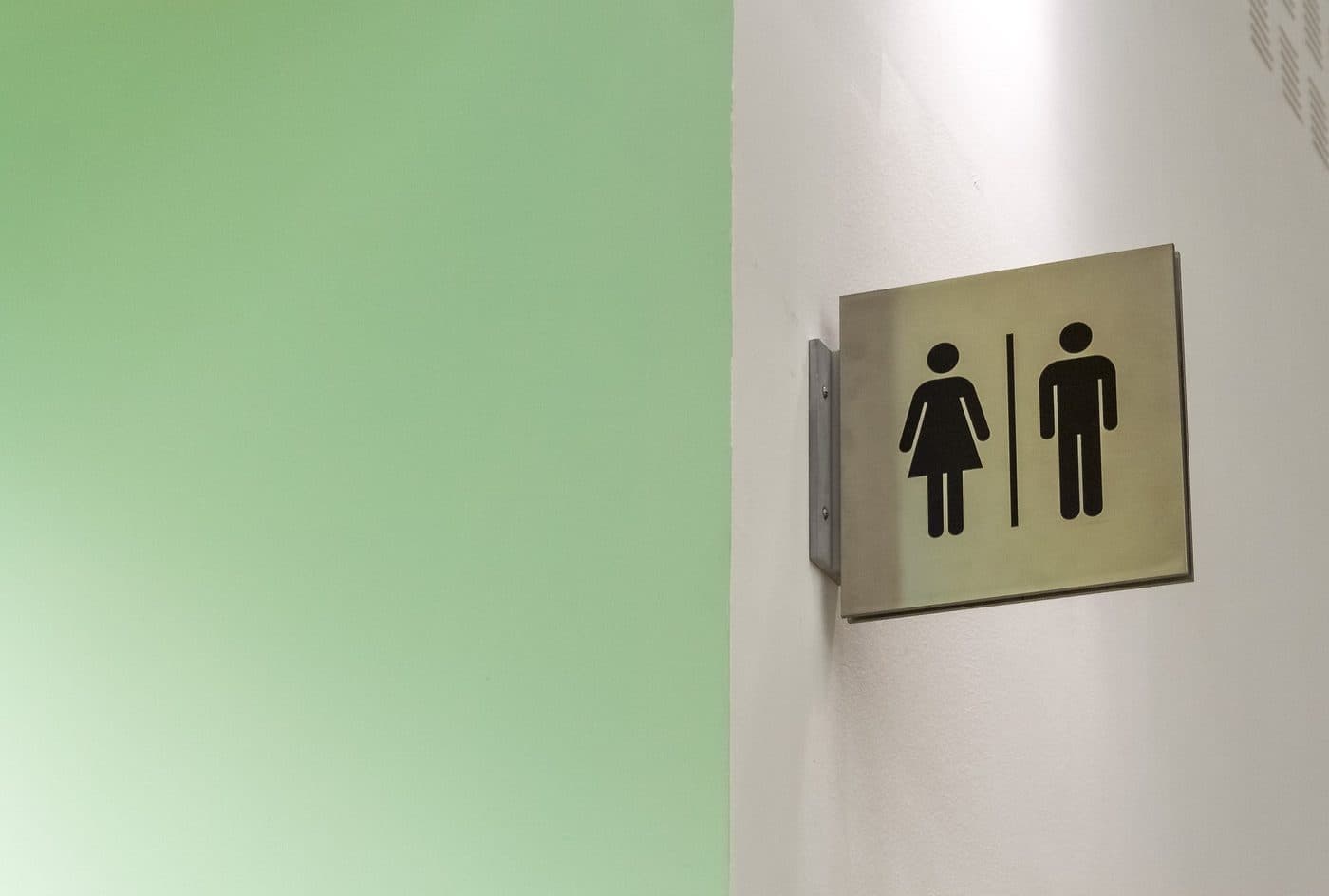 A restroom sign mounted on a bright hallway wall, representing urinary health and frequent trips to the bathroom