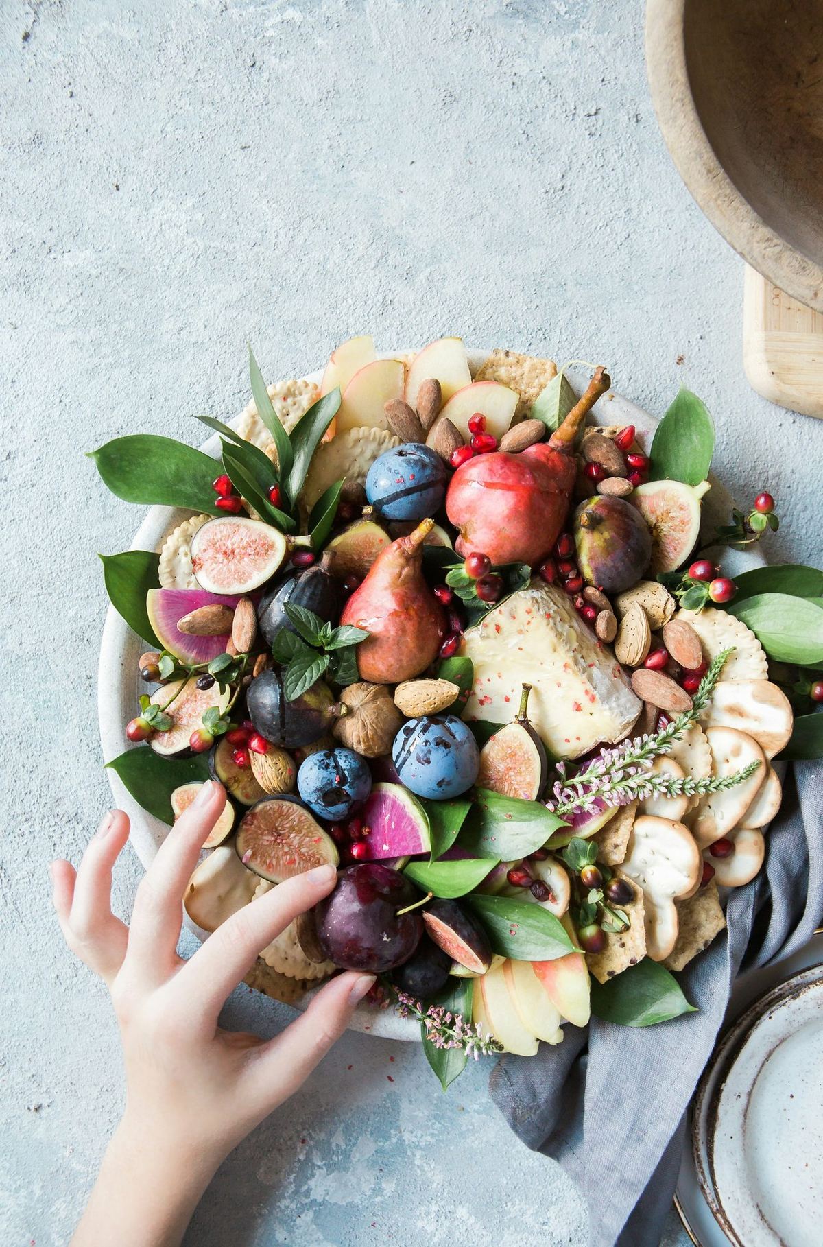 Overhead photo of a platter of fresh fruit, nuts, cheese and crackers with a hand reaching toward it, a reminder that everyday food choices sit at the center of blood sugar management.