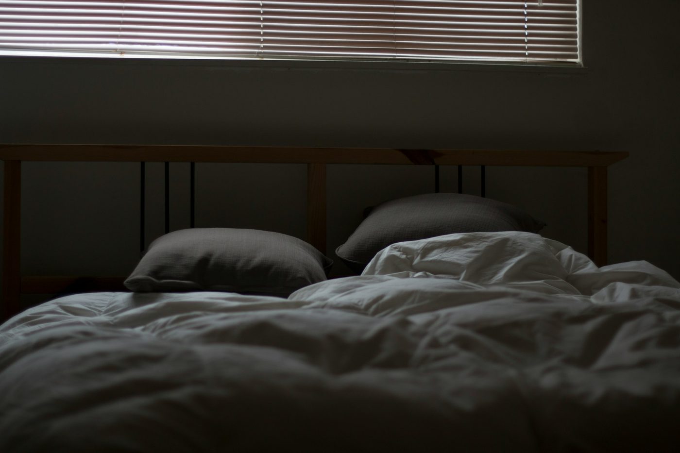 A dim bedroom with an empty, unmade bed and closed blinds, the scene many people know after a night of broken sleep.