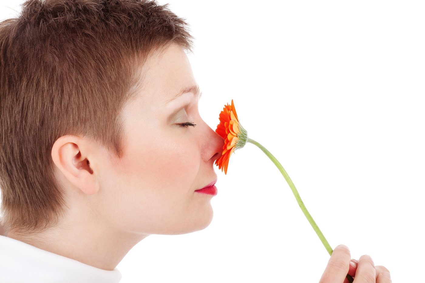 A person leaning in to smell a bright orange flower, a reminder that pollen is a common trigger for allergy and sinus symptoms.