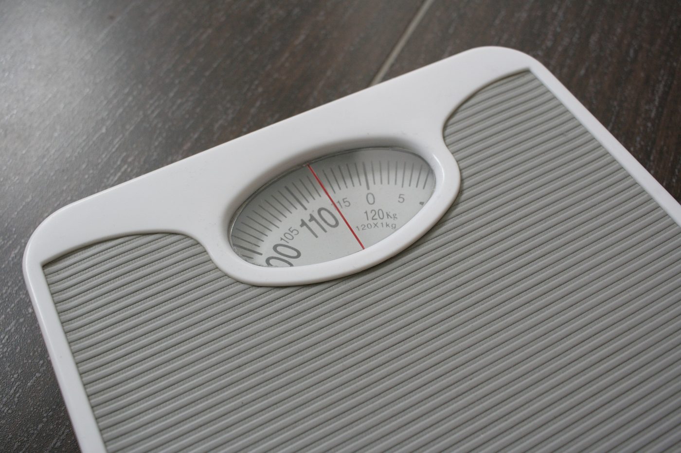 A simple bathroom scale on a wood floor, one of the tools used to track progress in a weight management plan.